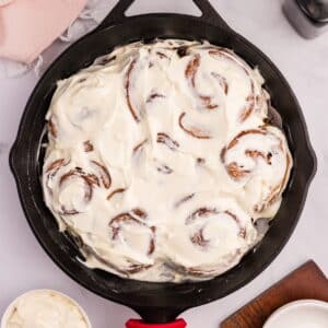 A cast iron skillet filled with cinnamon rolls topped with cream cheese frosting.