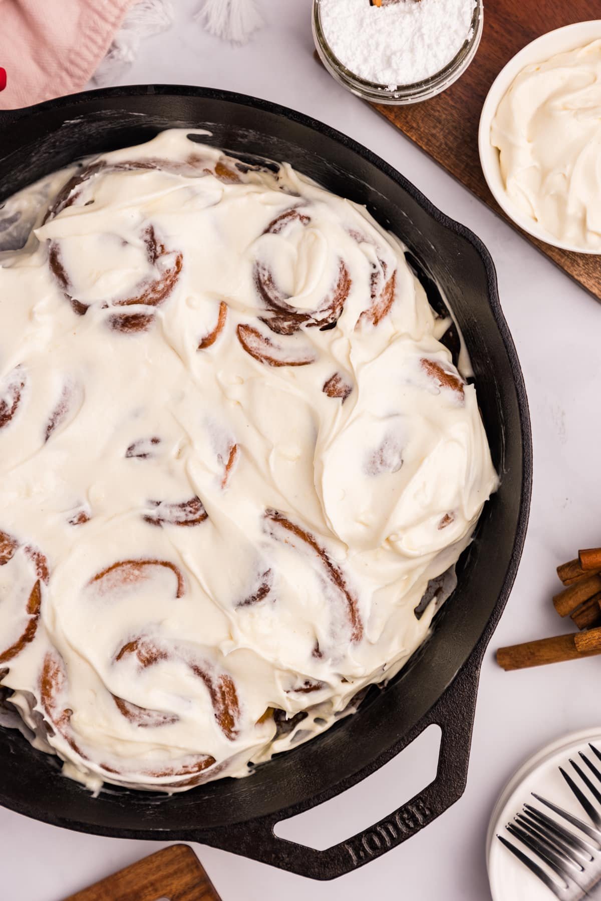 A cast iron skillet filled with cinnamon rolls that are topped with cream cheese frosting.