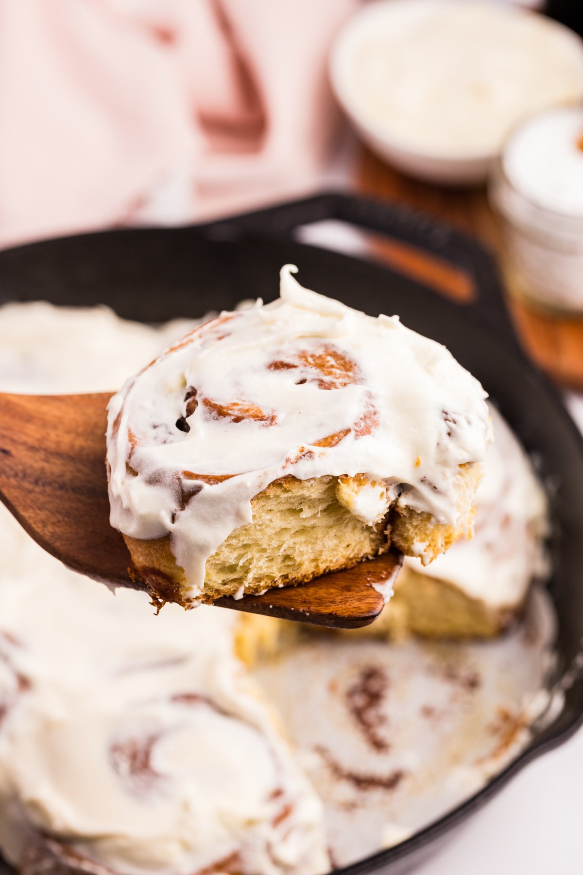 Lifting a cinnamon roll from a cast iron skillet.