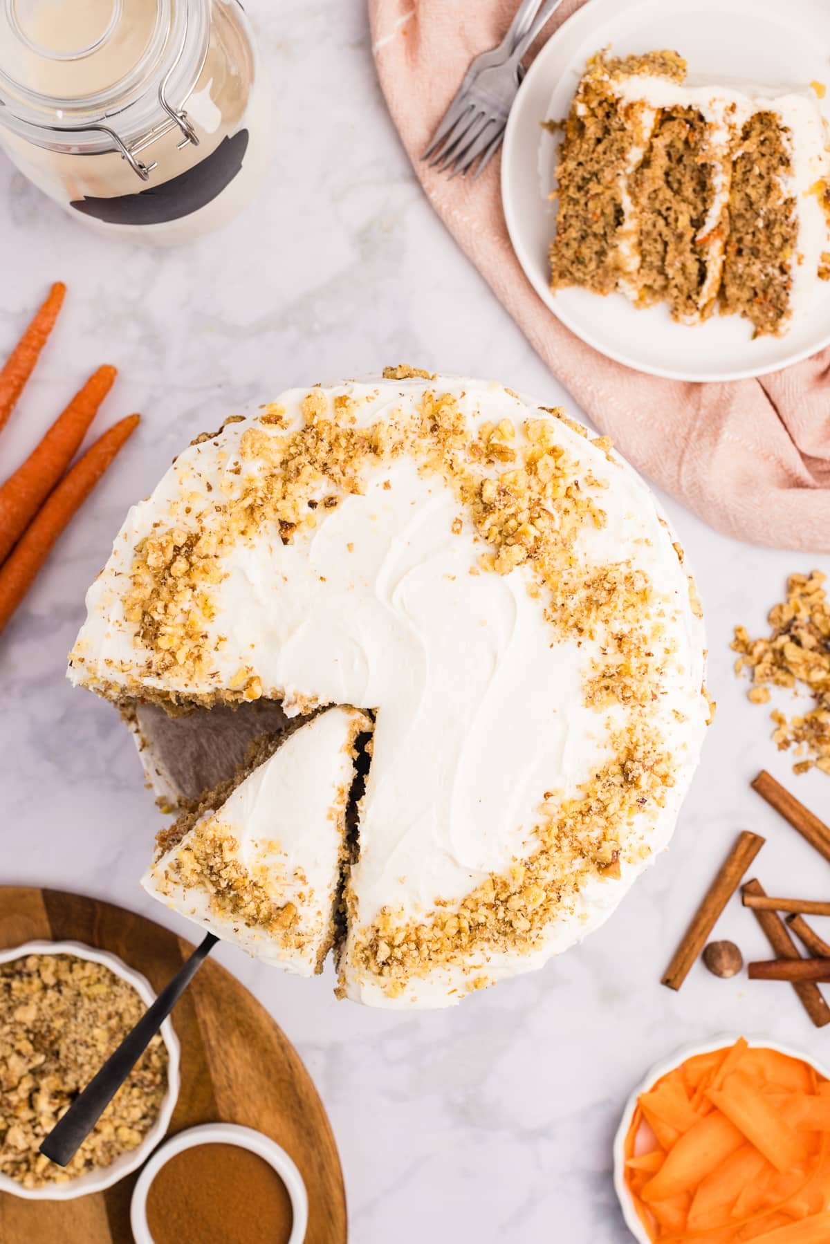 Removing a slice of cake from a large cake covered with cream cheese frosting and walnuts.