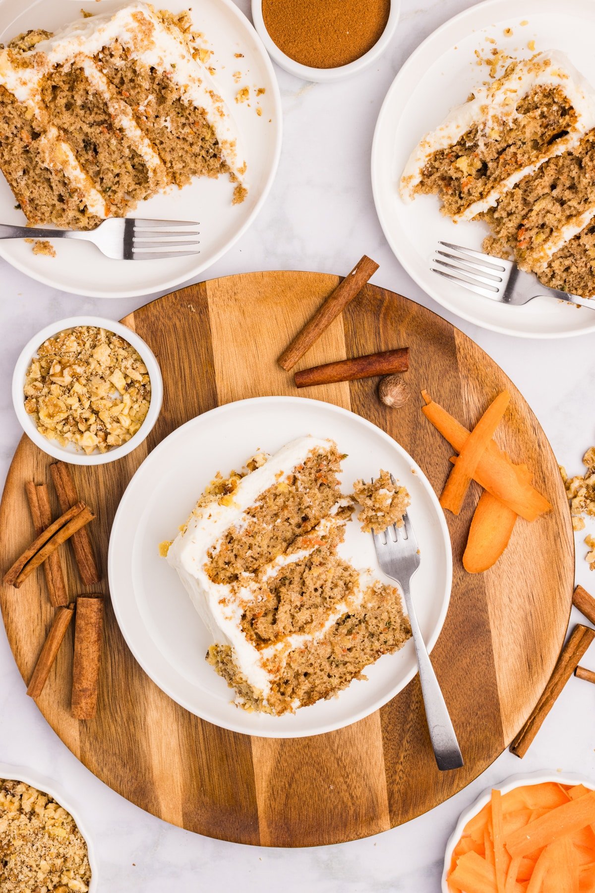 An overhead image of a slice of carrot cake on a plate, surrounded by various ingredients.