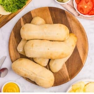 A pile of homemade sourdough sandwich rolls on a round wooden board.