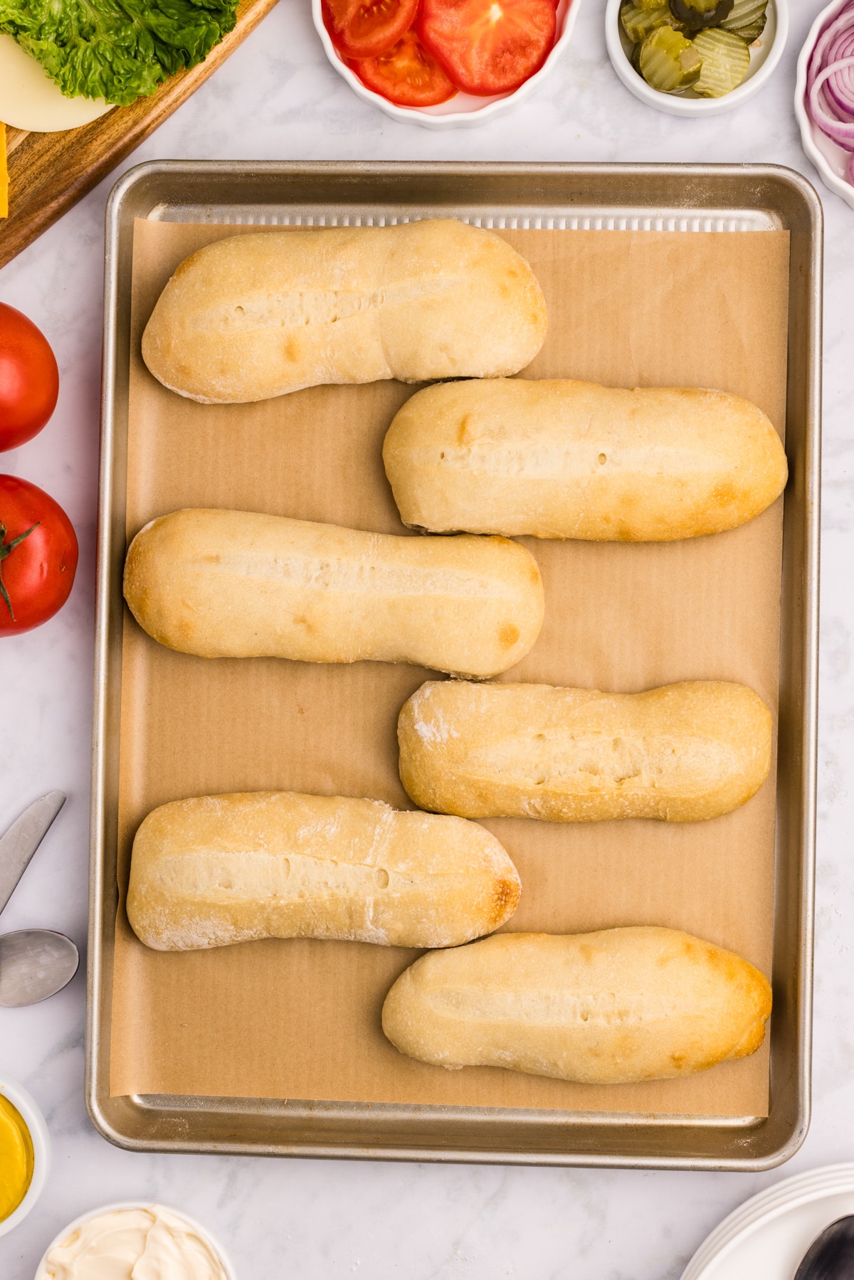 A baking sheet filled with homemade hoagie sandwich rolls.