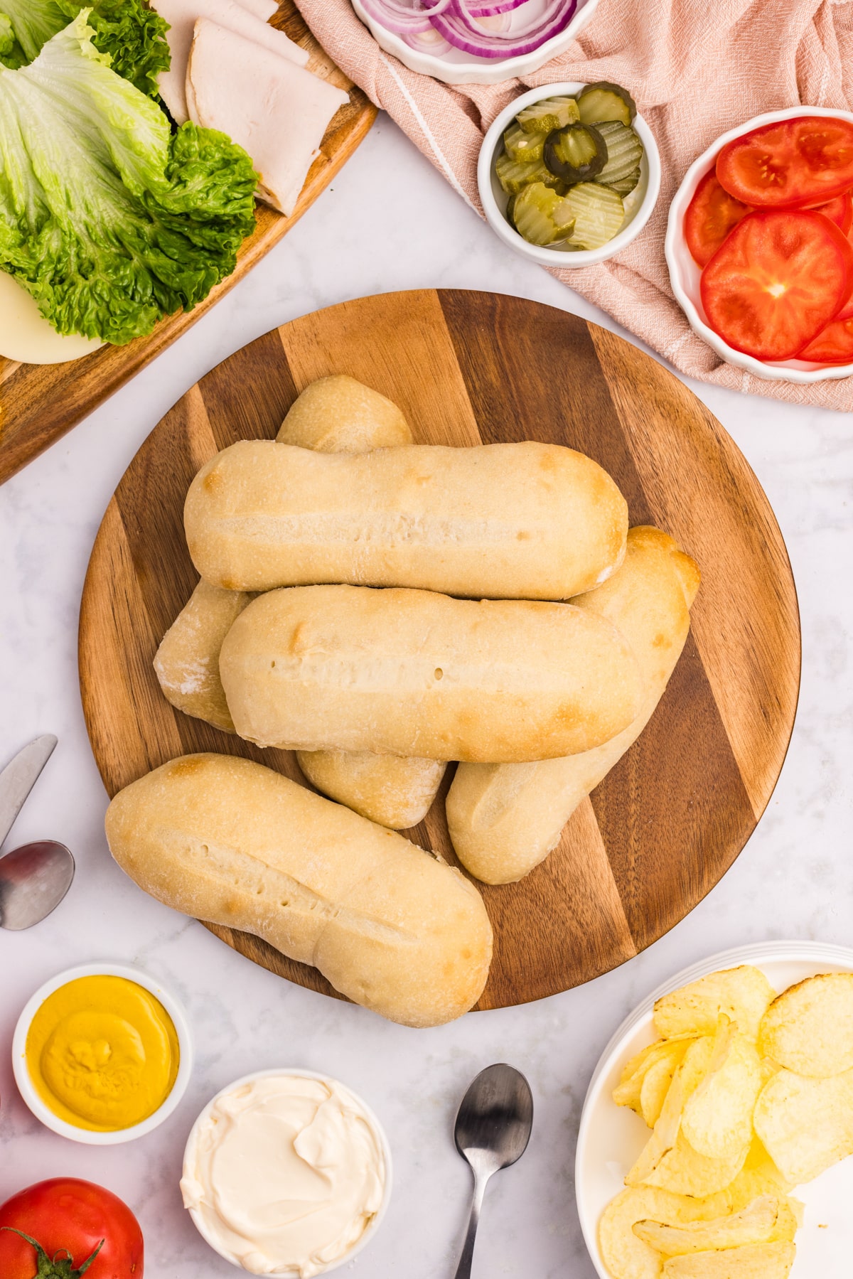 A pile of sandwich rolls on a round wooden cutting board.