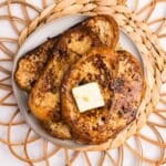 Three slices of french toast stacked on a plate, topped with a pat of butter, and drizzled with maple syrup.