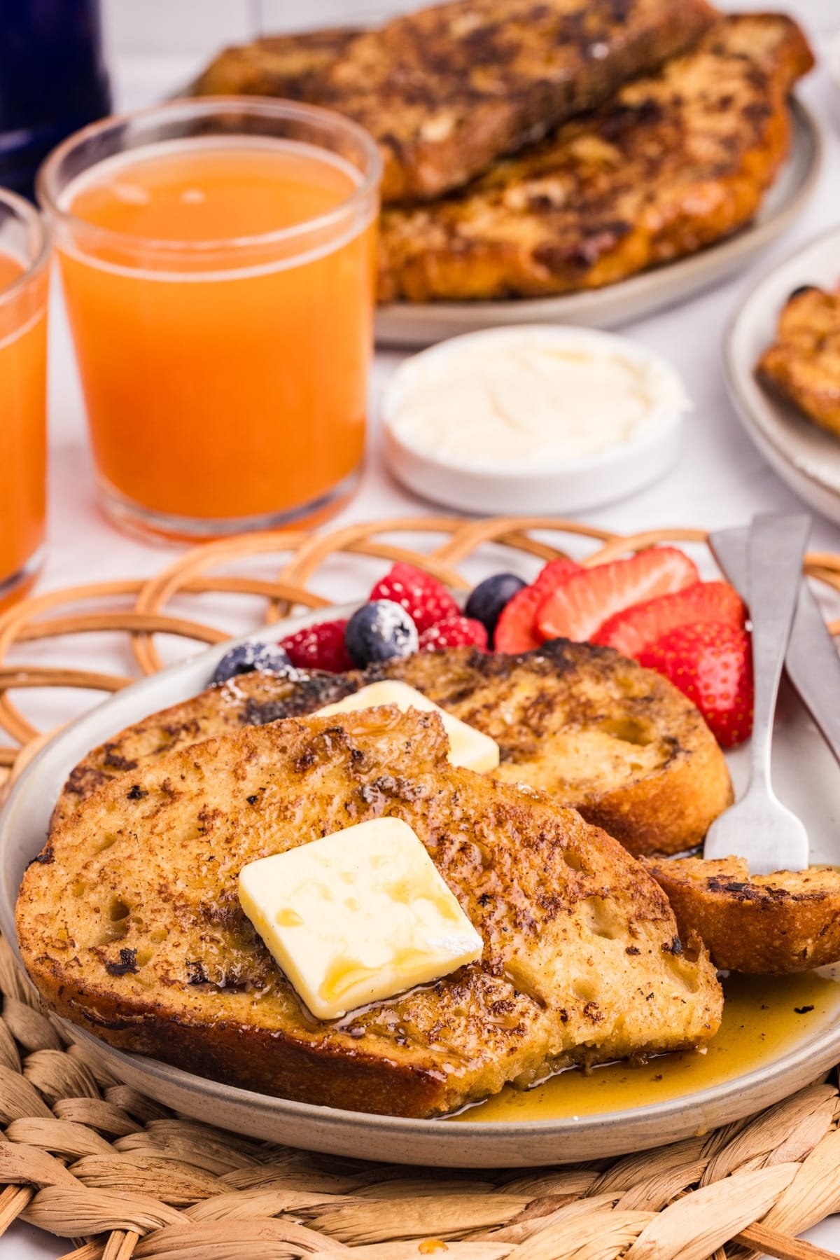 Multiple slices of french toast on a plate, topped with butter and drizzled with syrup.