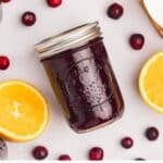 A jar of cranberry sauce with cranberries and orange on the counter.