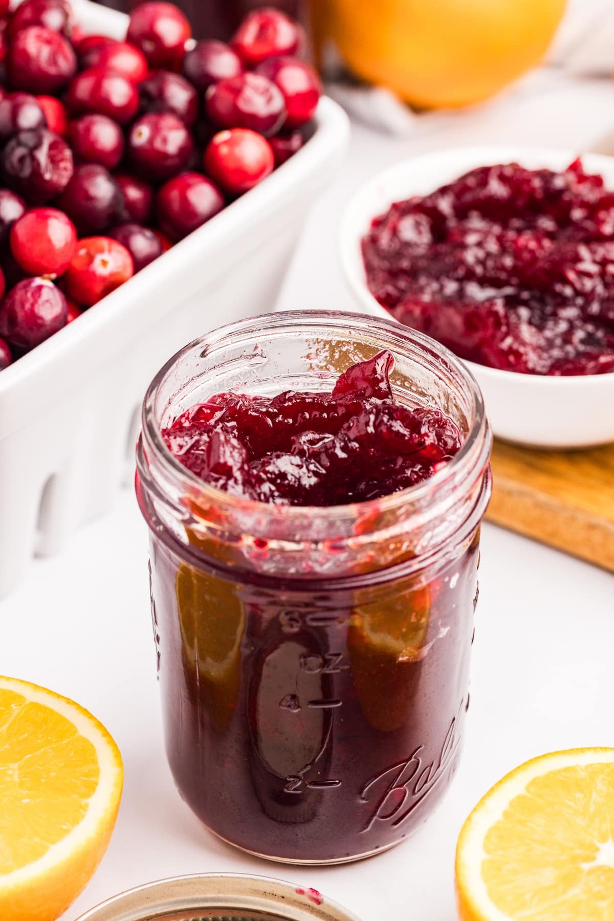 A jar of cranberry sauce with oranges around the side.