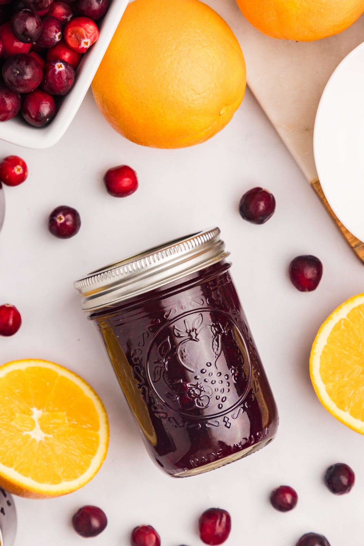 A jar of cranberry sauce surrounded by cranberries and oranges.
