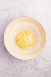 Adding grated butter to a bowl of dry ingredients.