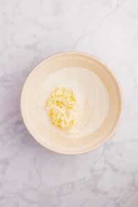 Adding grated butter to a bowl of dry ingredients.