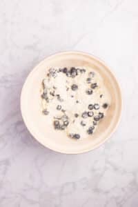 Adding blueberries to dry ingredients and stirring them until lightly coated in flour.