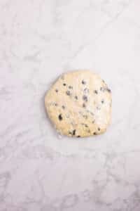 Blueberry scone dough wrapped tightly in plastic and shaped into a circle.