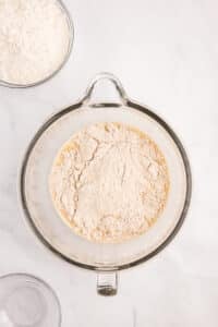 Adding whole wheat flour to a glass bowl.