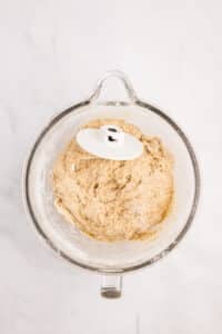 A wet dough in the bowl of a stand mixer with a dough hook attachment.