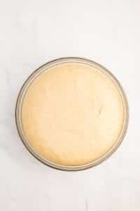 A bowl filled to the brim with proofed dough.