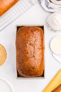 A loaf of baked bread in a loaf pan with a golden brown top.