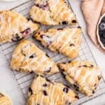 Blueberry scones on a wire rack, drizzled with lemon glaze.