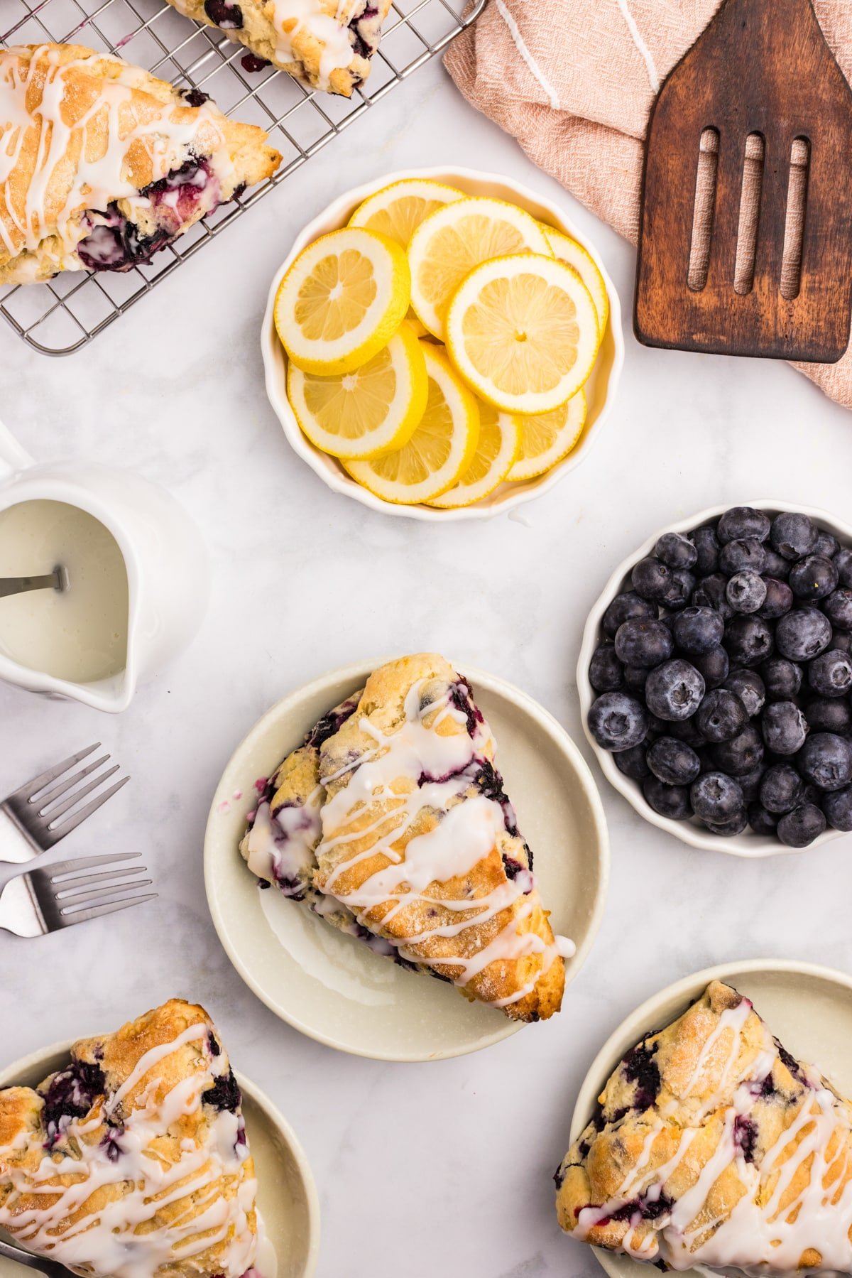 A scone on a plate, drizzled with a glaze and surrounded by fresh blueberries and lemon.