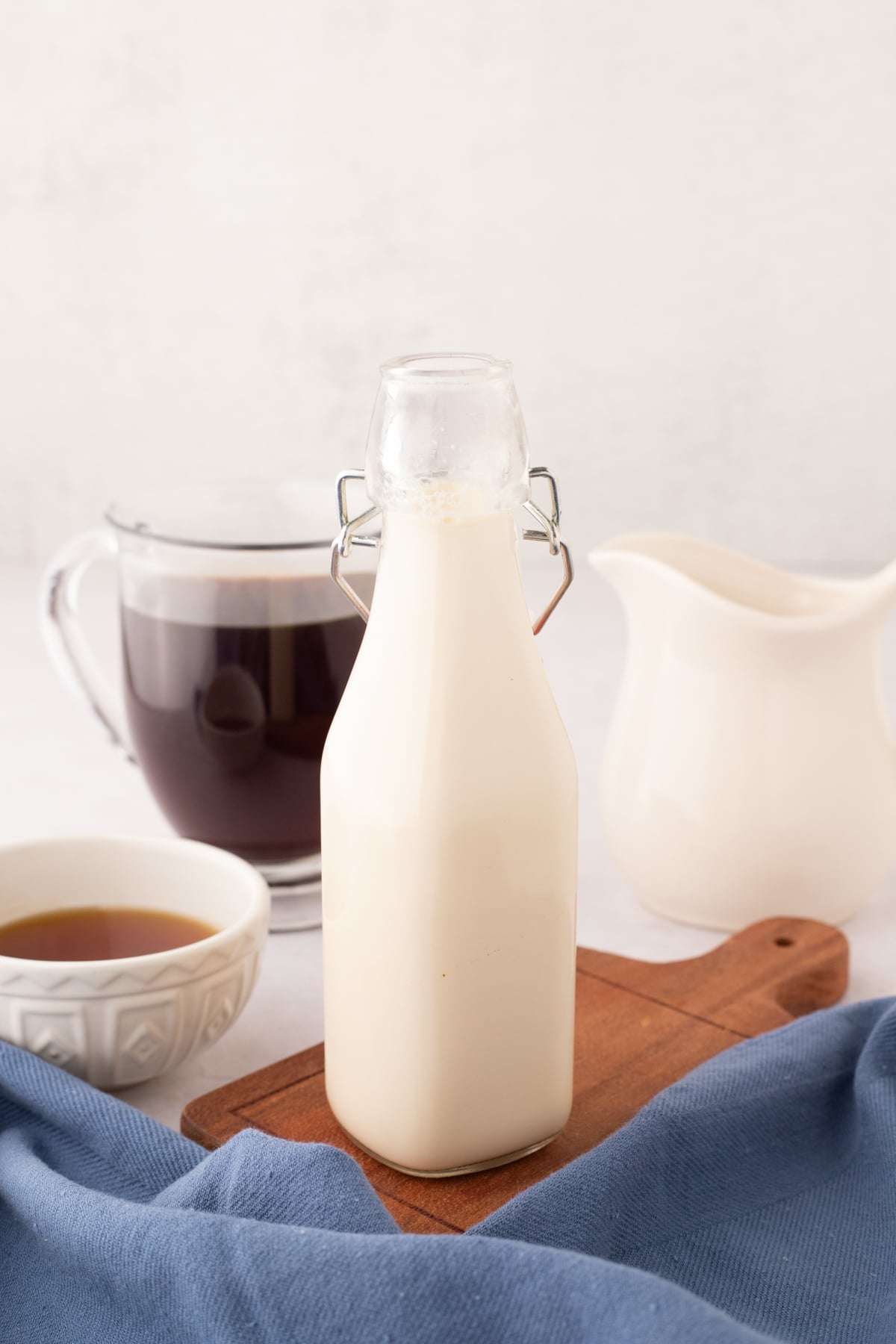 A bottle filled with homemade creamer, with a cup of coffee in the background.