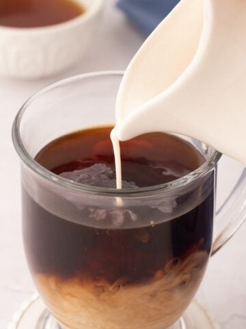 Pouring coffee creamer into a cup of coffee.