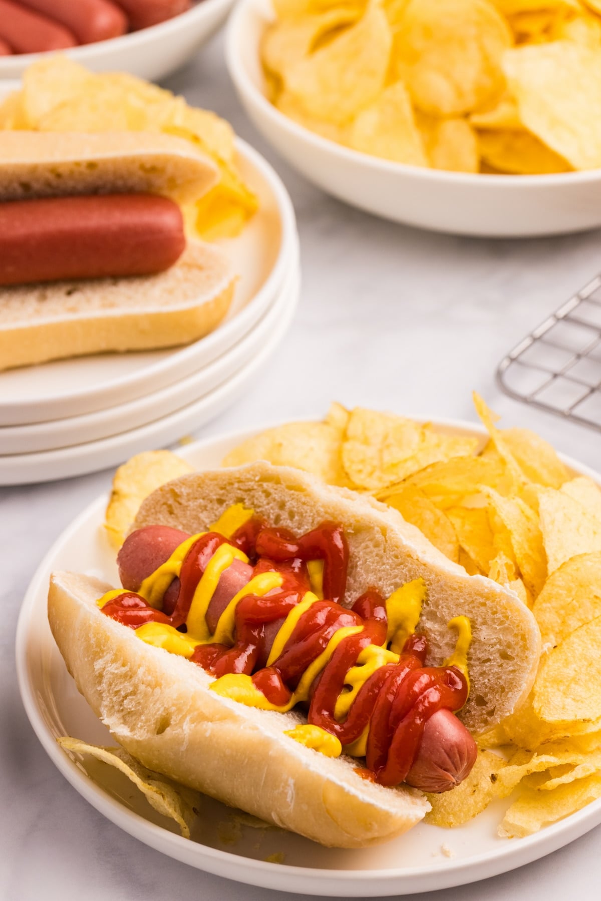 A hot dog served on a homemade bun with potato chips on the side.
