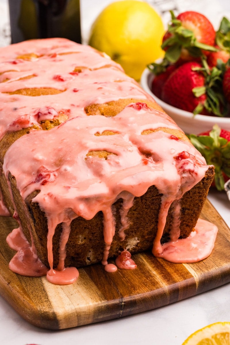 Strawberry glaze dripping down the sides of a loaf of quick bread.